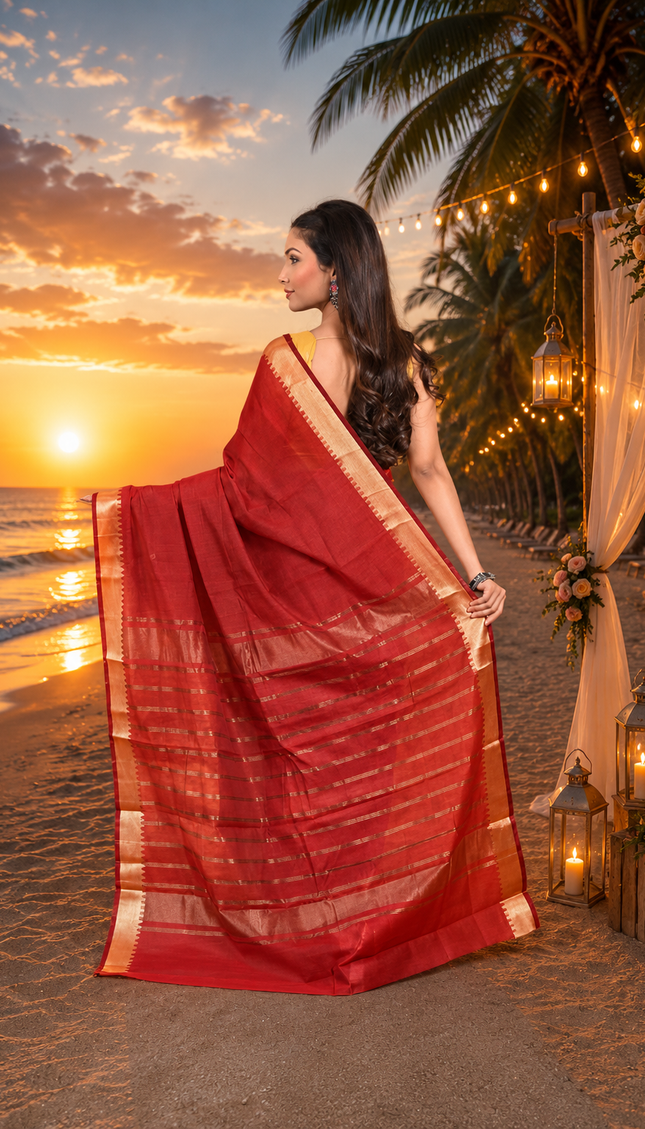 Model showing the back drape of a crimson Mangalgiri cotton saree with a handwoven golden zari border and striped pallu at a beachside sunset.