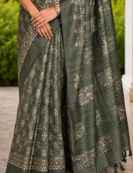Close-up of a green Tussar silk cotton saree showing white floral Batik print, patterned border, pleats, and tasseled pallu.