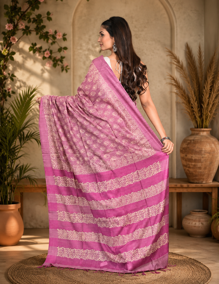 Back view of a woman displaying a mauve-lavender Tussar silk cotton saree with delicate white Batik floral print and magenta striped border in a courtyard.