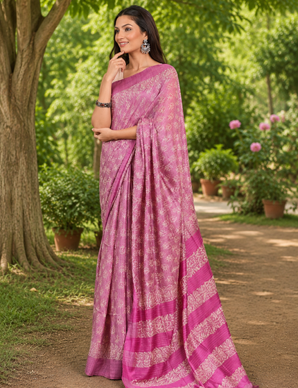 Three-quarter view of a woman wearing a mauve-lavender Tussar silk cotton saree with delicate white Batik floral print and magenta border, standing on a sunlit garden path.