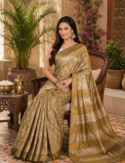 Woman seated wearing an olive cotton silk Batik saree with cream floral buti motifs and patterned pallu in a courtyard