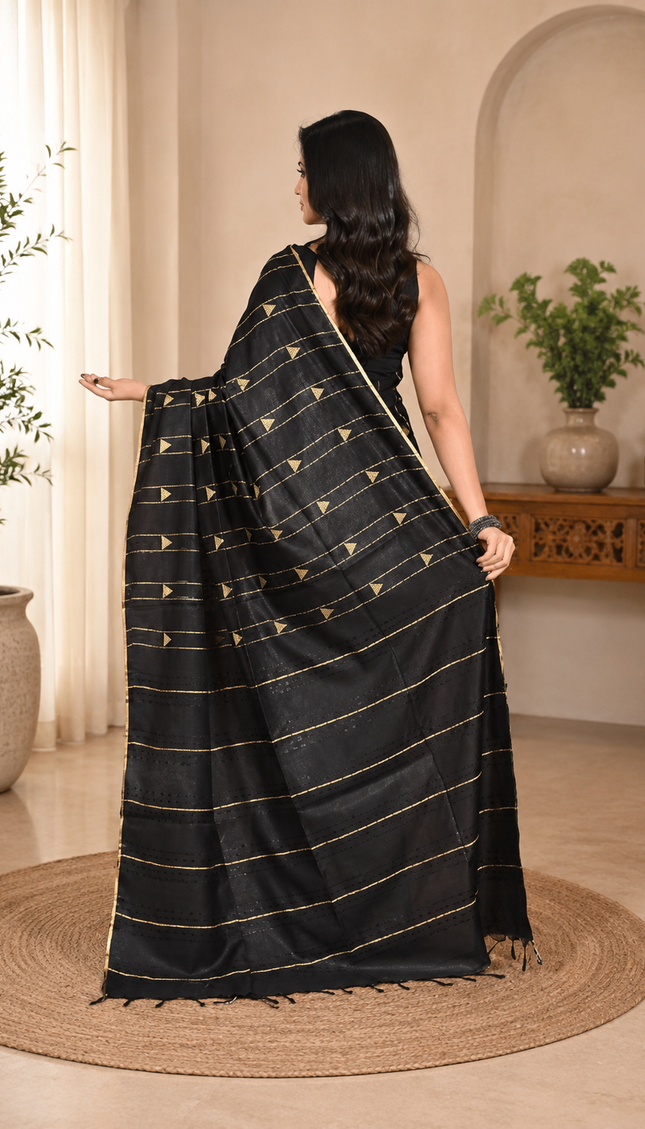Back view of a model wearing a black cotton saree with horizontal gold stripes indoors