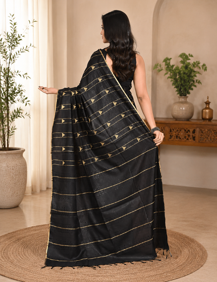 Back view of a model wearing a black cotton saree with horizontal gold stripes indoors