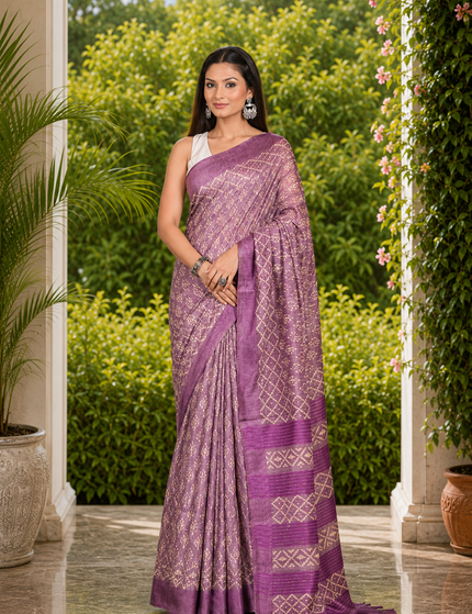 Woman wearing a light plum Tussar silk cotton saree with delicate geometric Batik pattern and darker plum striped border, standing in a sunlit garden courtyard.