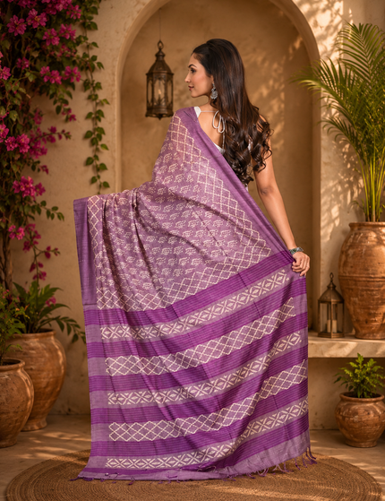 Back view of a woman displaying a light plum Tussar silk cotton saree with delicate geometric Batik pattern and darker plum striped border in a warm arched courtyard.