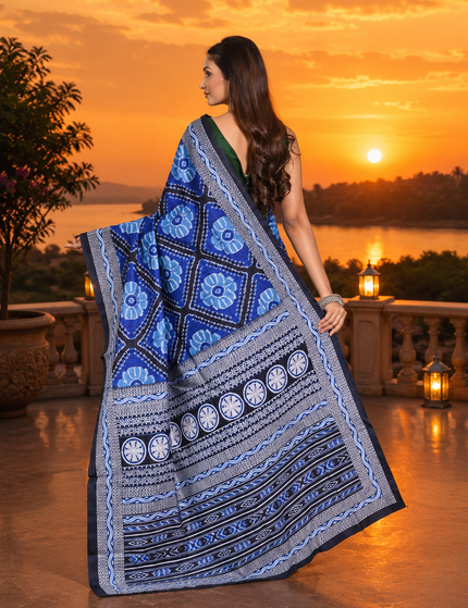 Model showing the back drape of a royal blue mercerized Ikkat silk saree with blue floral motifs, black-and-white patterned borders, circular details, and striped pallu at sunset.