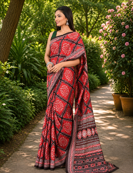 Model wearing a red mercerized Ikkat silk saree, three-quarter front view showing geometric motifs, circular floral patterns, striped pallu, and black-and-white borders on a garden path.