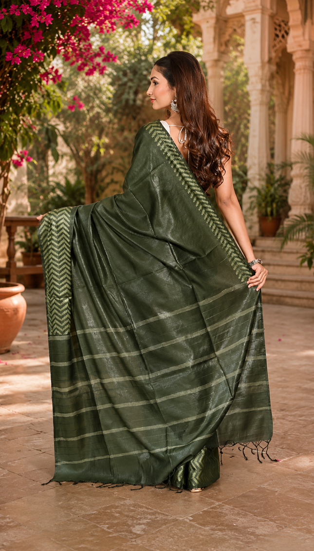 Back view of a woman displaying a bottle green cotton Fishbone saree with a zigzag herringbone border and striped pallu in a sunlit courtyard.