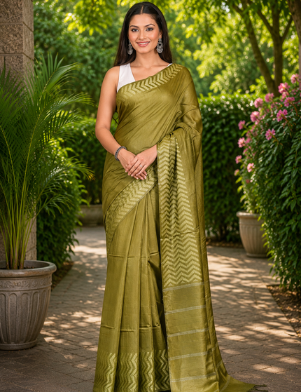 Woman wearing an olive green cotton Fishbone saree with a zigzag herringbone border and striped pallu, standing in a sunlit garden.