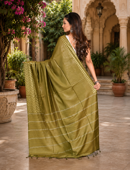 Back view of a woman displaying an olive green cotton Fishbone saree with a zigzag herringbone border and striped pallu in a sunlit courtyard.