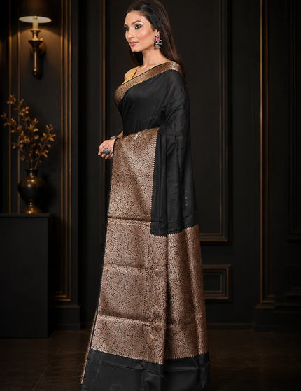 Model wearing a black cotton zari saree with a golden patterned border and pallu, three-quarter front view in an elegant dark interior.