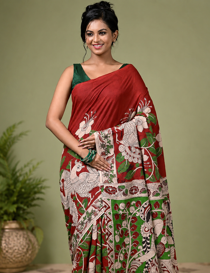 Mid-length portrait of a model in a red and green Kalamkari digital print cotton saree, showing white bird motifs, floral details and green blouse.