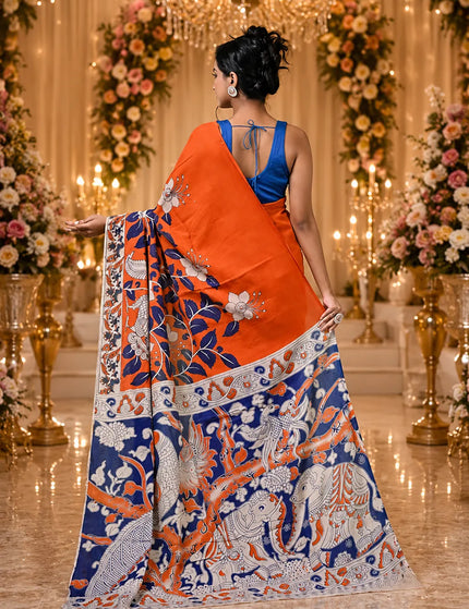 Model showing the back of an orange and navy Kalamkari digital print cotton saree, with a wide patterned pallu and decorative border.