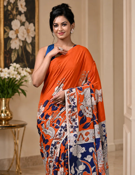 Close-up of a model wearing an orange and navy Kalamkari digital print cotton saree, highlighting floral, bird and figurative motifs.