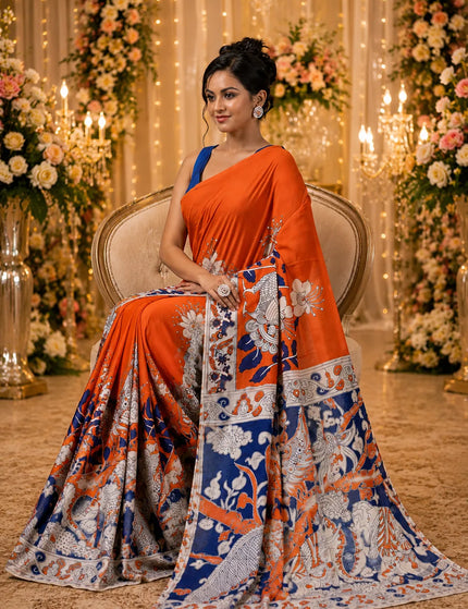 Model seated in an orange and navy Kalamkari digital print cotton saree, showing the patterned pallu, figurative motifs and decorative border.