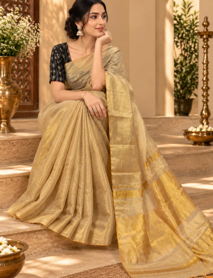 Seated model wearing ivory Mull cotton saree with golden border and tasseled pallu